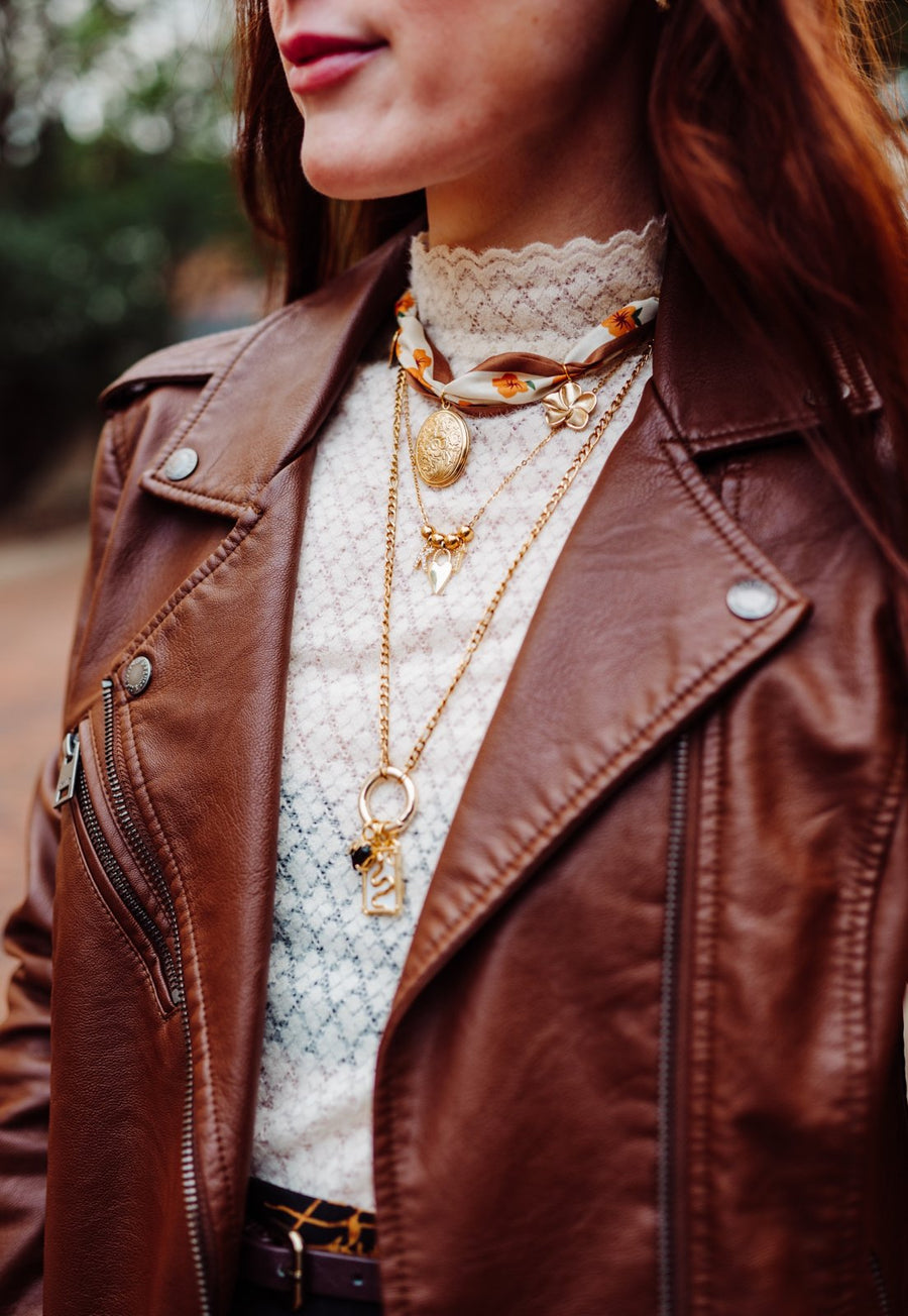 Layered gold charm necklaces with a floral locket and silk scarf over a cream lace top