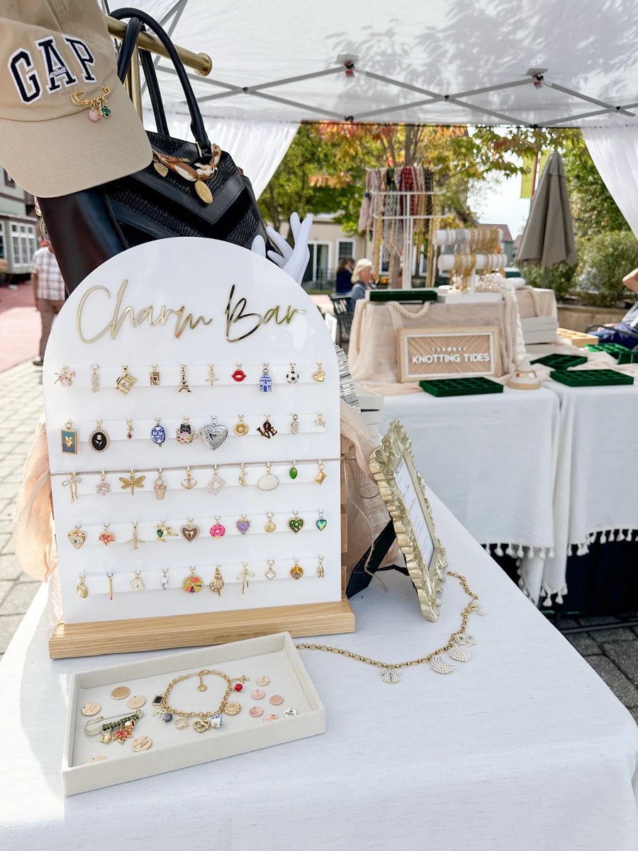 White arched Charm Bar board lined with charms at an outdoor market